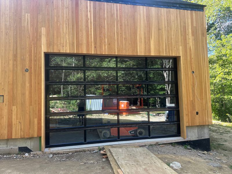 Full-view aluminum and glass garage door installed on modern cedar building in Massachusetts