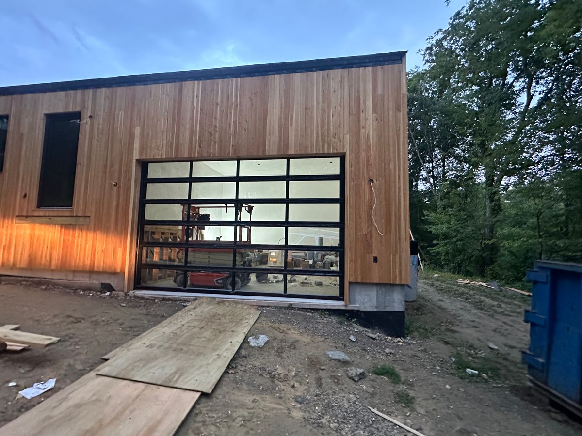 Full-view glass garage door on modern cedar-clad building at dusk — MA custom project